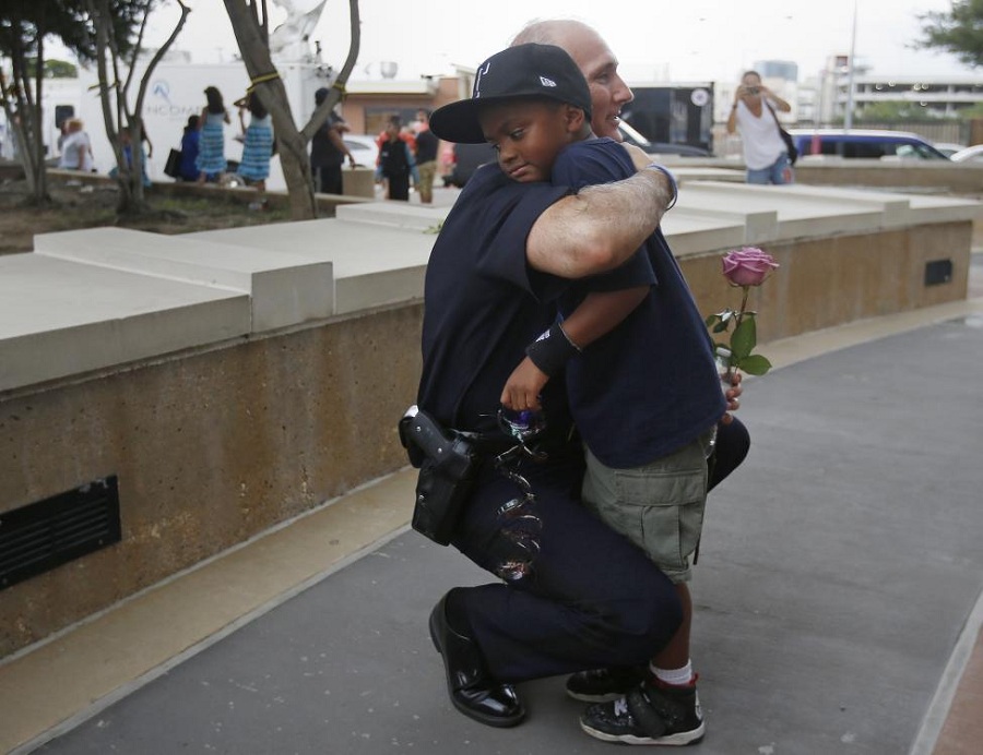 A Dallas Police officer hugs a child who came to pay respects at a makeshift memorial at Dallas Police Headquarters following the multiple police shootings in Dallas. REUTERS/Carlo Allegri