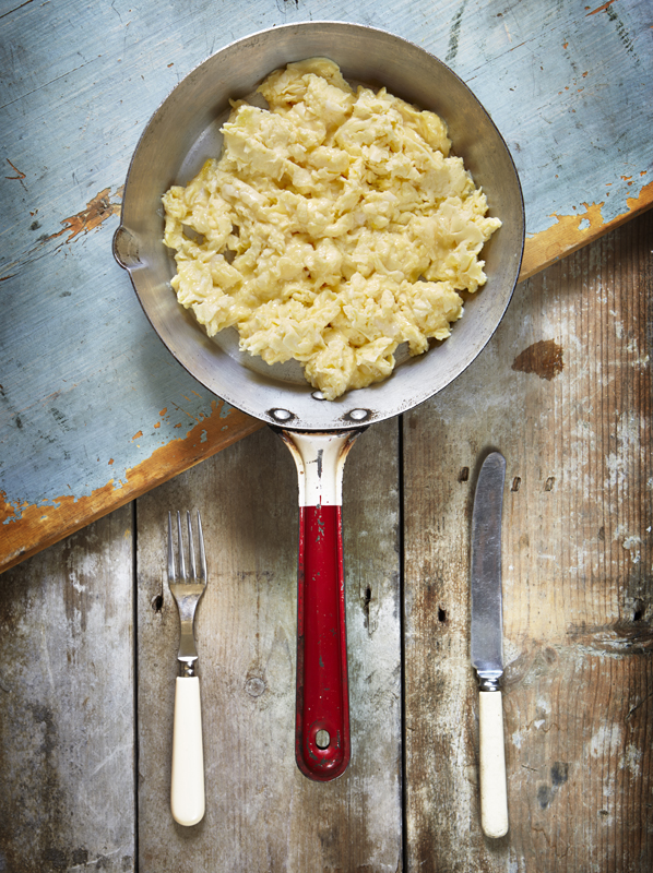 Scrambled eggs in a frying pan with a knife and fork on a wooden kitchen worktop