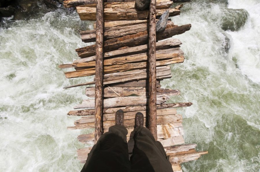 A point of view shot looking down of trekker crossing the swollen Kanka River on a rickety wodden bridge, Naranag, Gangabal Lake region, Kashmir Himalayas, India