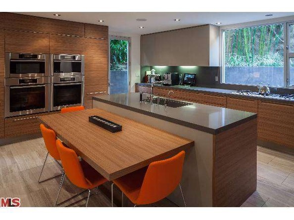  تمامی کابینت های آشپزخانه و جزیره آن از جنس چوب هستند و برای ایجاد تنوع، از صندلی های نارنجی برای میز ناهار خوری استفاده شده.