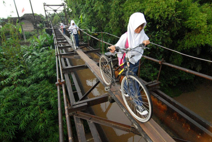 CENTRAL JAVA, INDONESIA - MARCH 11, 2014: Indonesian students go to school via suspension bridge that connects the Suro village and Plempungan village on March 10, 2014 in Boyolali, Central Java, Indonesia. The series of iron rods along the length of 30 meters and a width of 1.5 meters which is located 10 meters above the Pepe river is actually not a bridge, but the irrigation canals that drain water from the Cengklik reservoir to the surrounding rice fields. Built in the Dutch colonial period, people then use it as a bridge by adding sheets of wood over metal rods that ran above the water line. Students escape the danger while passing. (Photo by Agoes Rudianto/Anadolu Agency/Getty Images)