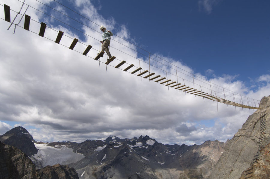 A woman crosses a bridge on a via ferrata in the Rocky Mountains in Canada. The via ferrata is on Mt. Nimbus, a peak only accissible via helicopter with Canadian Mountain Holidays.