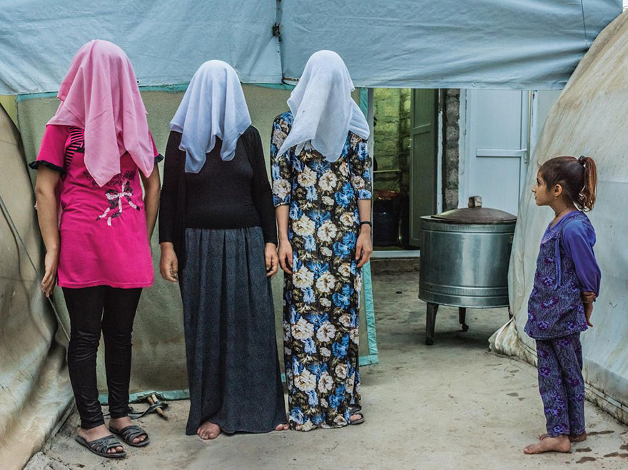 24- دخترک در حال تماشای سه زن کرد است که صورت خود را با روسری هایشان پوشانده اند. آنها بیان داشته اند که پیش از فرار و پناه بردن به چادر پناهندگان، نیروهای داعش آنها را مجبور به ازدواج کرده بوده اند.
