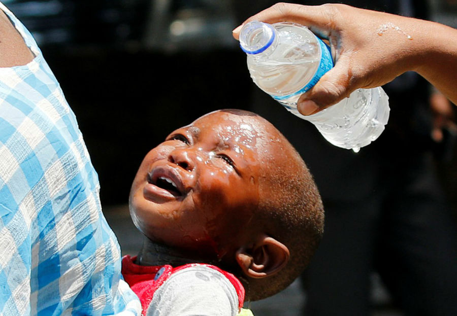 زنی در حال ریختن آب بر صورت کودکی که از گازهای اشک آور شلیک شده توسط نیروهای پلیس در حراره در زیمباوه آسیب دیده است.