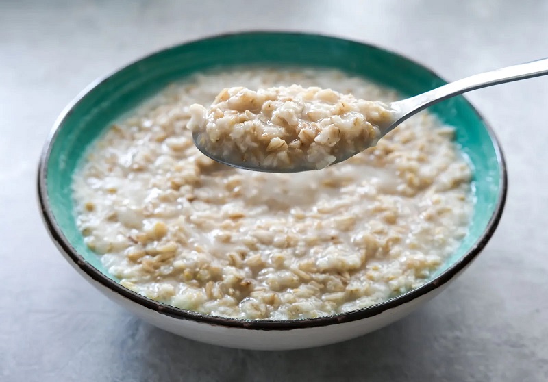 11 spoon held over bowl of cooked oats porridge